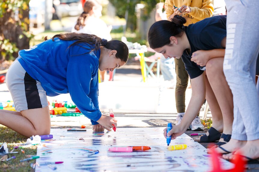 An image of two teenage girls kneeling over while drawing on a banner outdoors