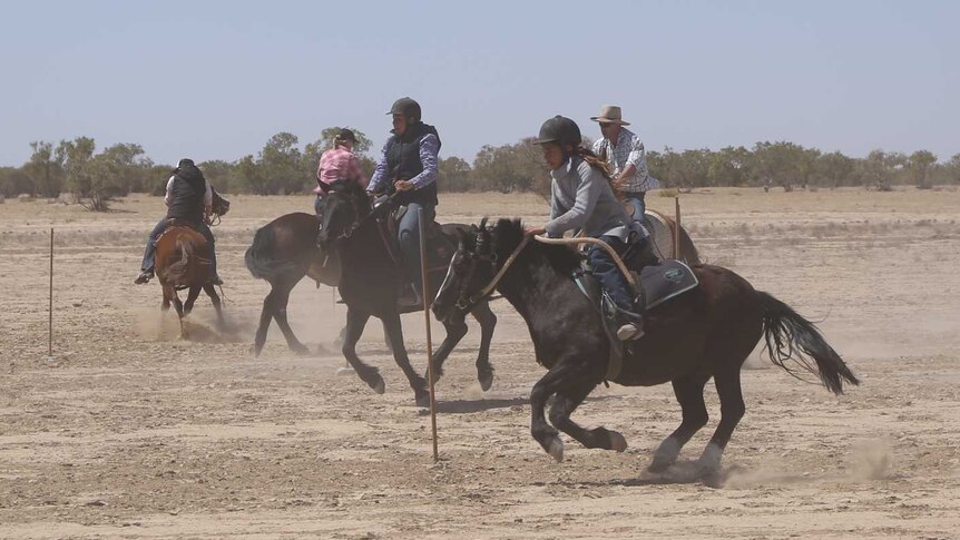 Horses run around a dusty race track