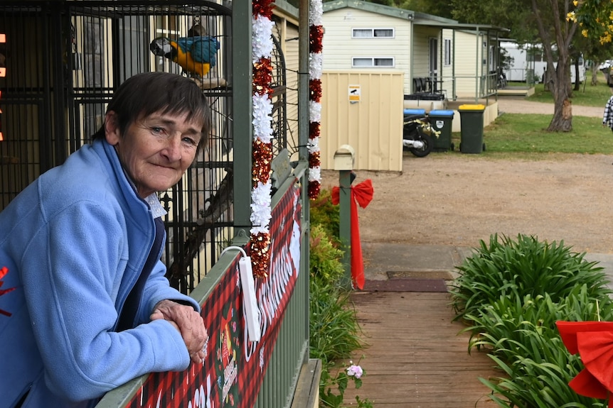 A woman leans on a porch fence with caravan park cabins in the background