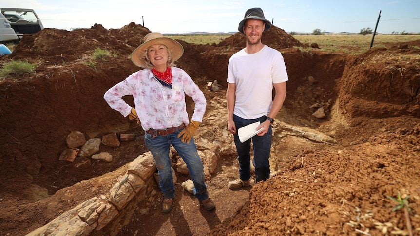 Two people stand smiling next to fossil