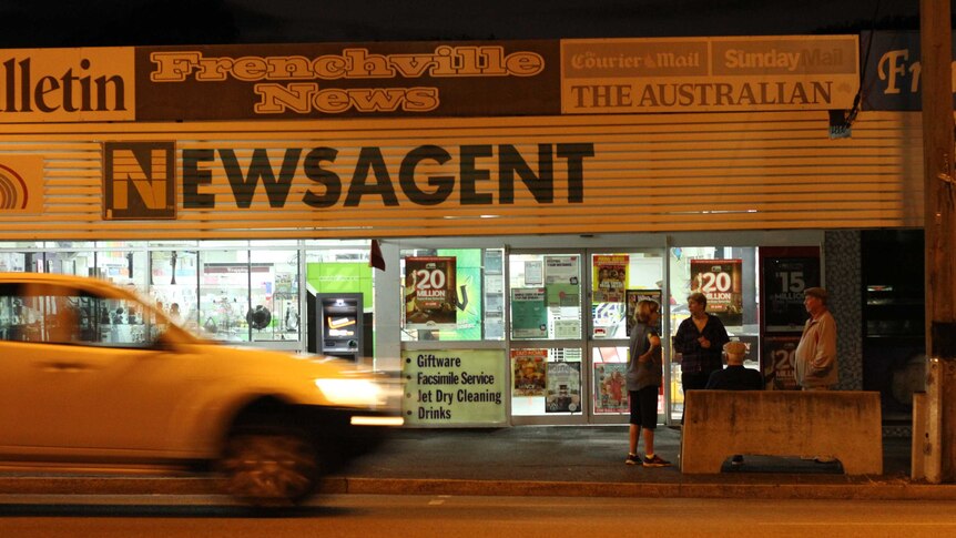 A group of people outside a newsagency just before dawn