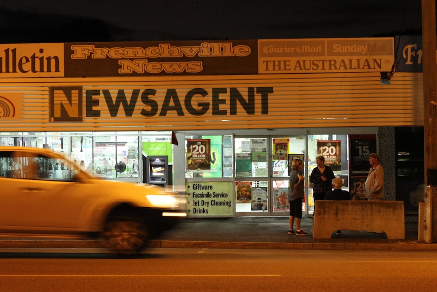 A group of people outside a newsagency just before dawn