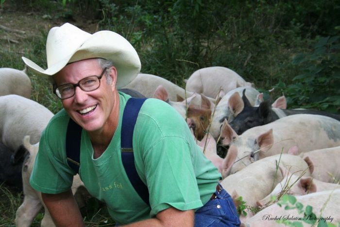 Farmer Joel Salatin crouched down surrounded by free range pigs.