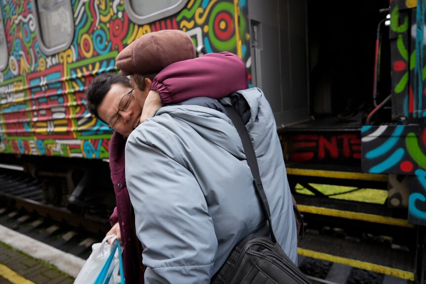 Two people hugging next to a train. 