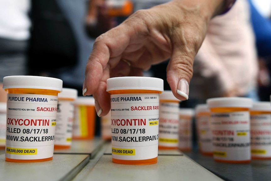 A woman reaches for a bottle of the opioid OxyContin.