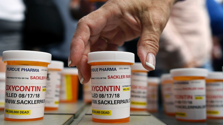 A woman reaches for a bottle of the opioid OxyContin.