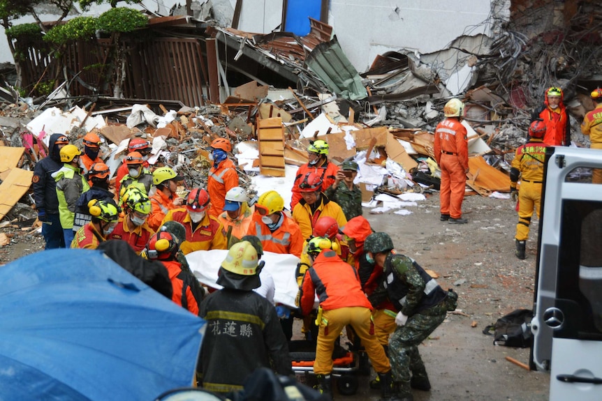 Workers wearing fluro jackets and helmets carry a victim from the Marshal Hotel.