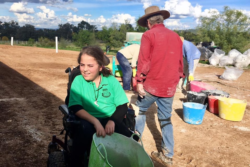 A girl in a wheelchair holding a green bucket