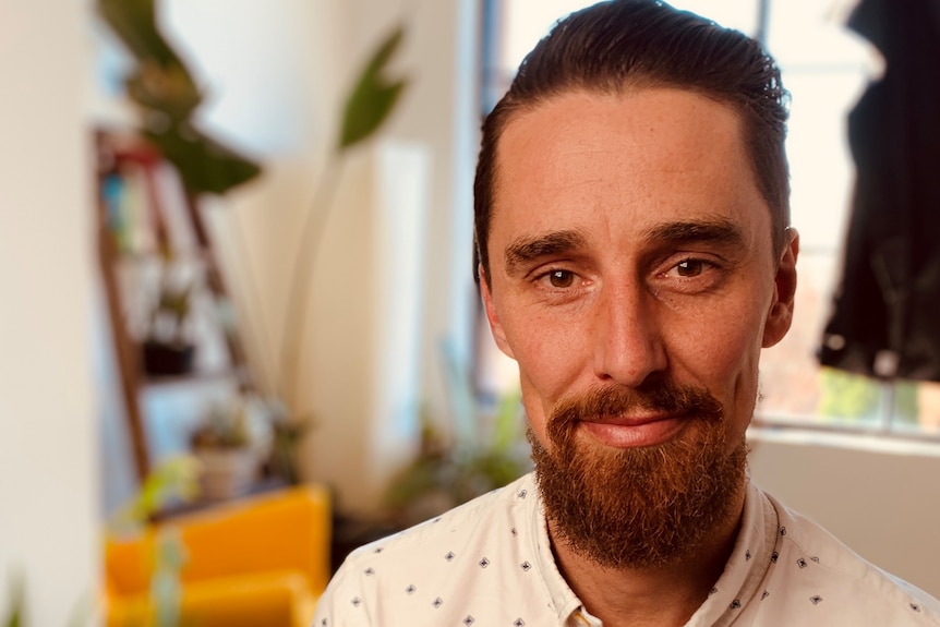 A man with a beard looks at the camera