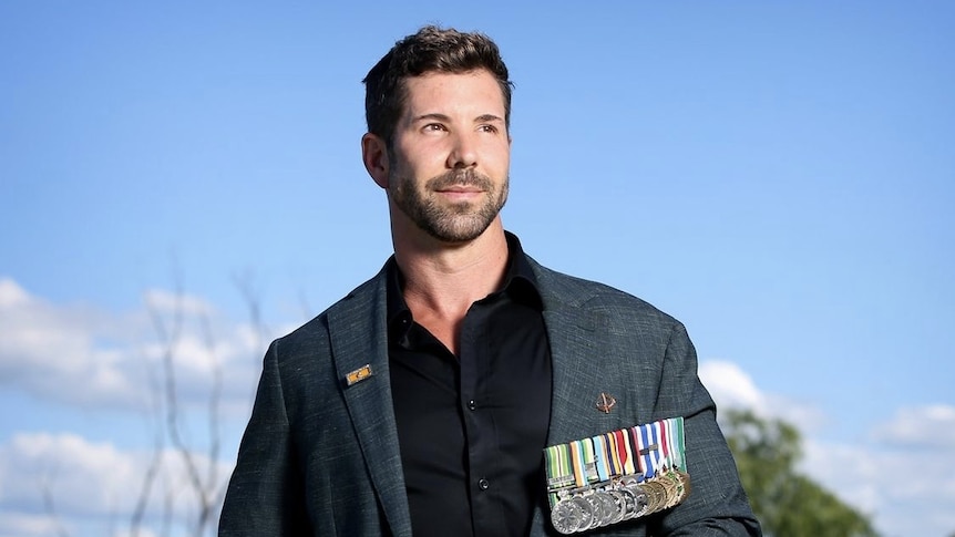 Heston Russell is poses for a portrait outside wearing a sports jacket with military medals pinned to his chest.