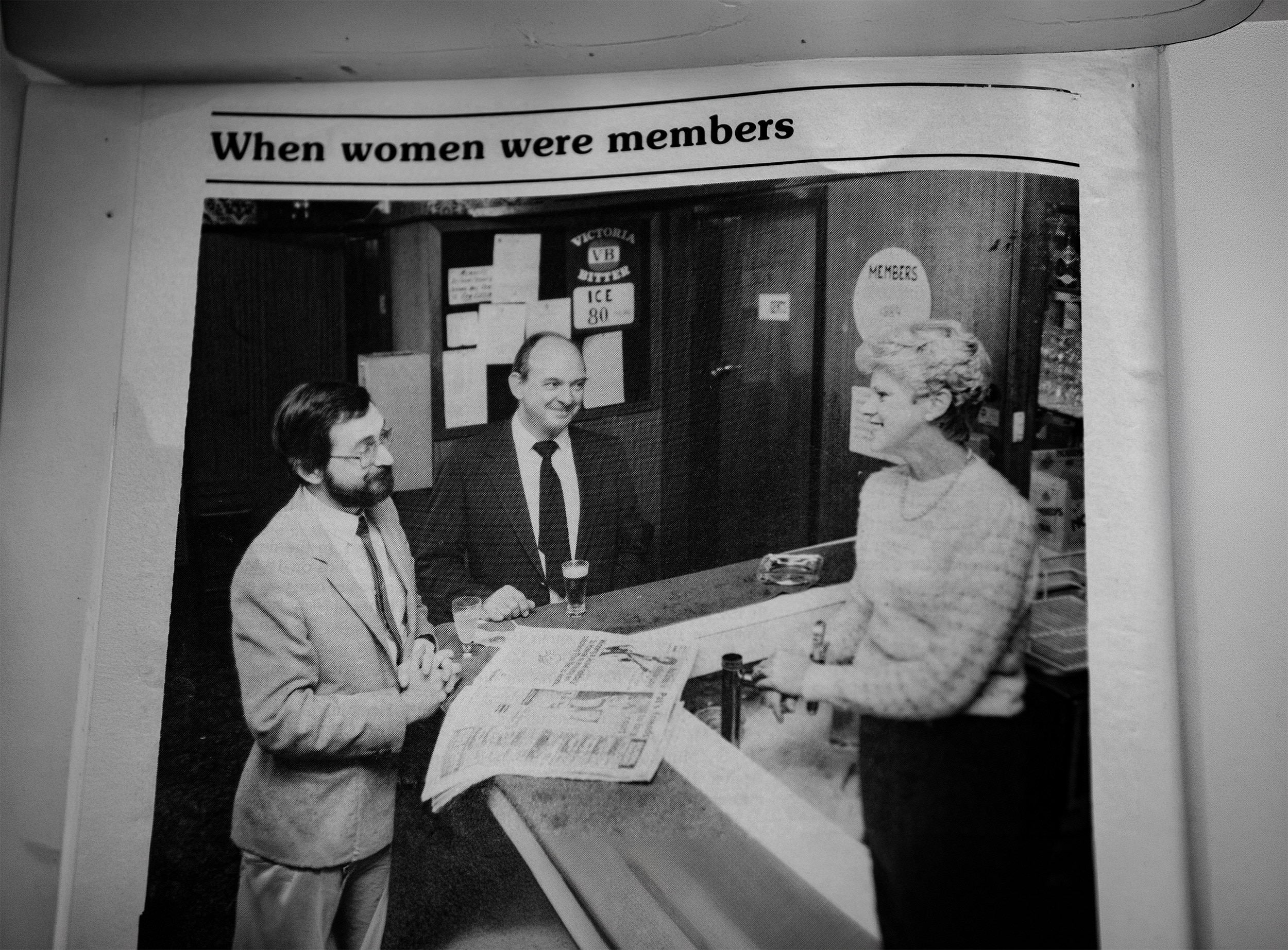 An old black and white magazine photo of two men talking to a woman over a bar