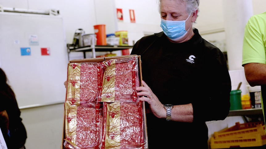 A masked man in a dark shirt holding up a big tray of mince.