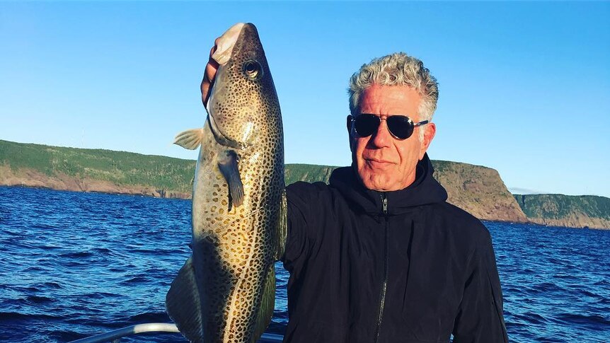 Anthony Bourdain holds up a long fish on a boat.