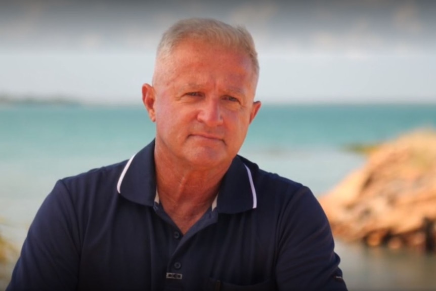 A man in a collared shirt, in front of a beach