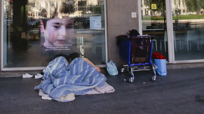 Homeless person sleeps under blanket in Italy