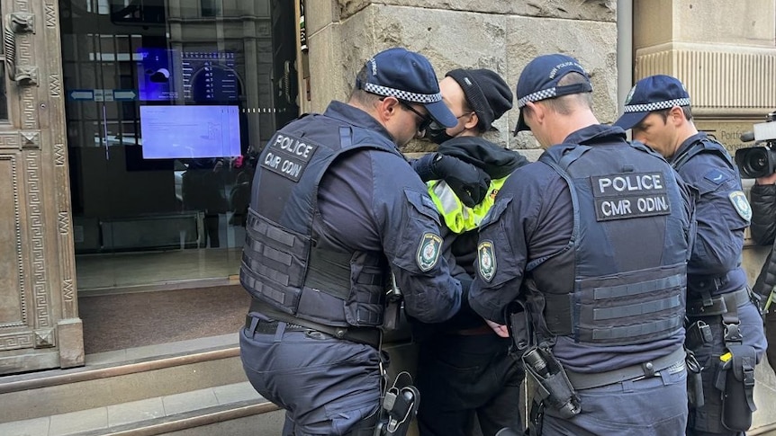 a person is held while three police officers place handcuffs on the person