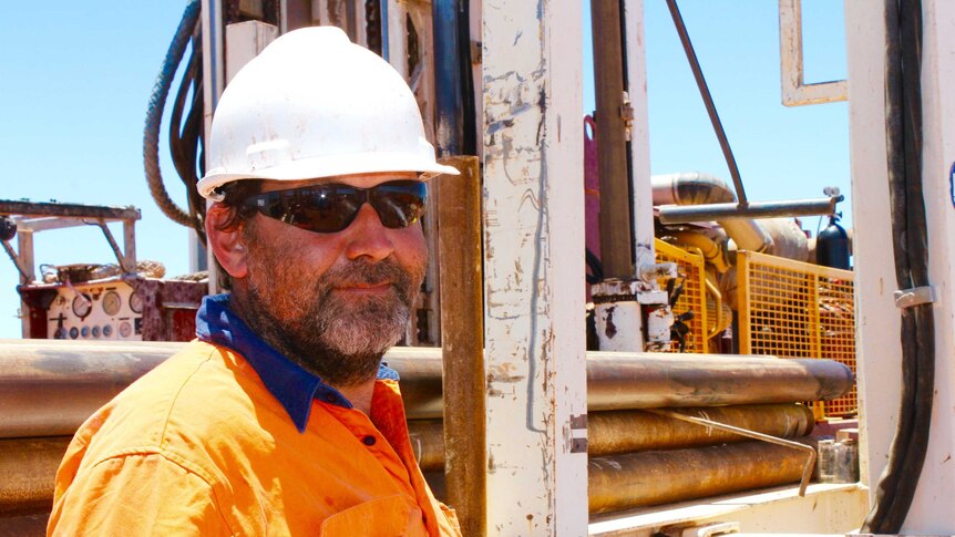 Profile shot of bore driller Jake Stratford. Standing in front of a drill rig wearing a high-vis shirt and white hard-hat