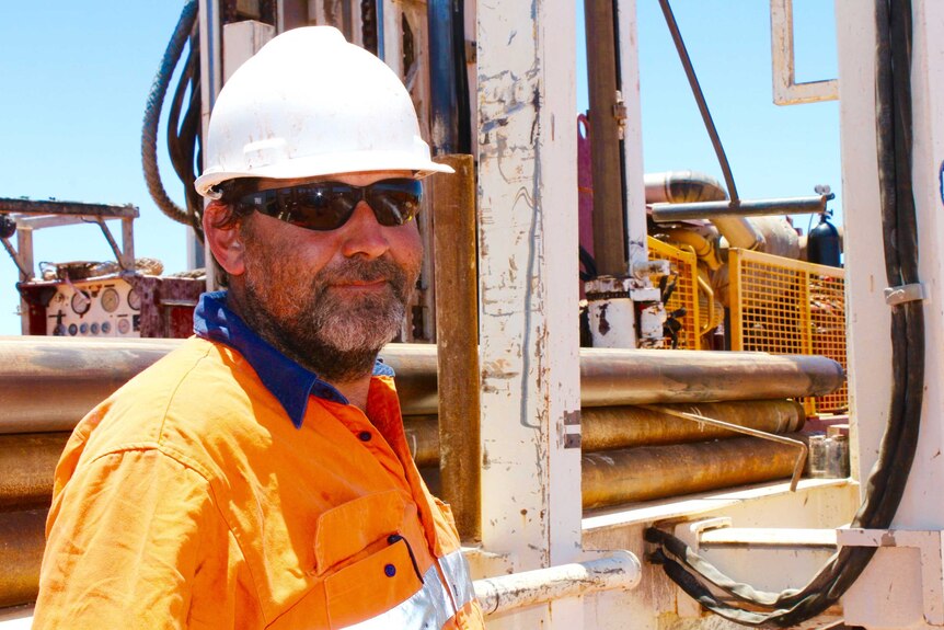 Profile shot of bore driller Jake Stratford. Standing in front of a drill rig wearing a high-vis shirt and white hard-hat