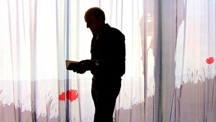 Silhouette of man holding small book with red poppy and soldier's shadow in background