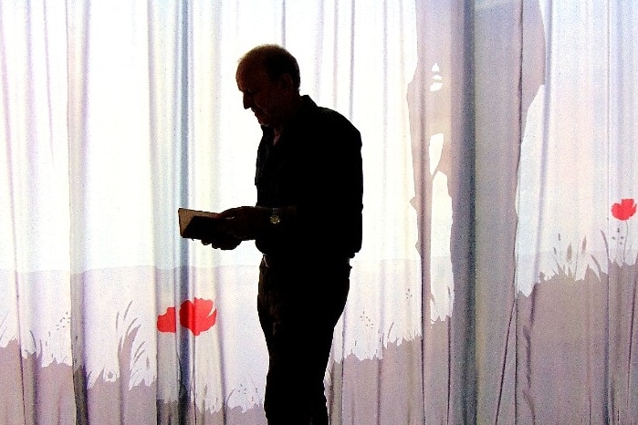 Silhouette of man holding small book with red poppy and soldier's shadow in background
