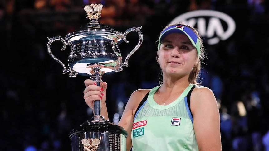 A cap-wearing tennis player holds a big trophy after winning her first Grand Slam title.