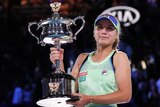 A cap-wearing tennis player holds a big trophy after winning her first Grand Slam title.