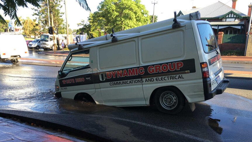 A van with its front wheels sinking into a deep puddle after a water main burst.