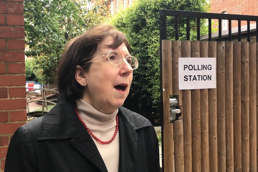 A woman stands on the street outside a polling station in London.
