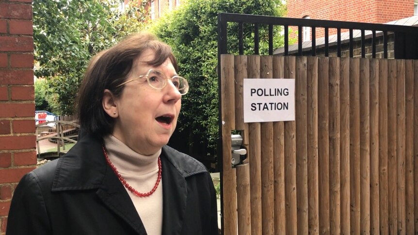 A woman stands on the street outside a polling station in London.
