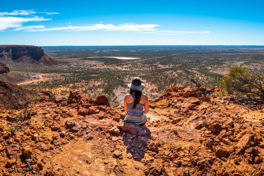 A woman sits on a mountain top in the Kennedy Ranges in a story about tourism to regions affected by natural disasters.