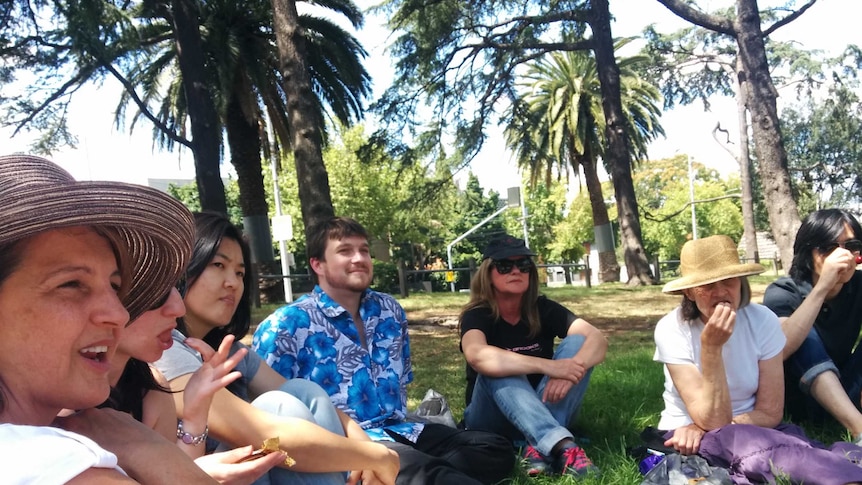 A group of people sit in a circle on the grass in a park.