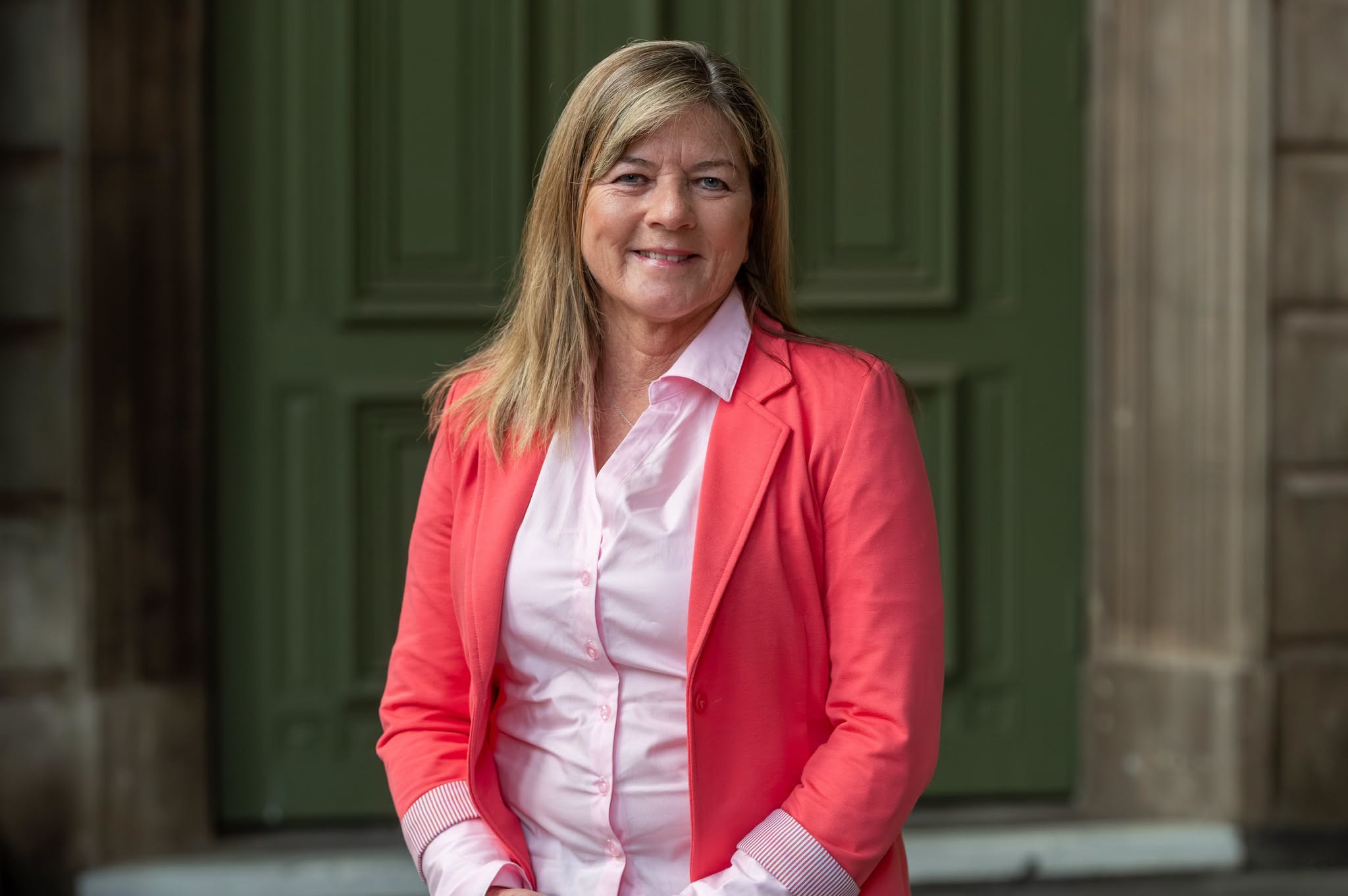 A woman in a pink shirt and blazer.