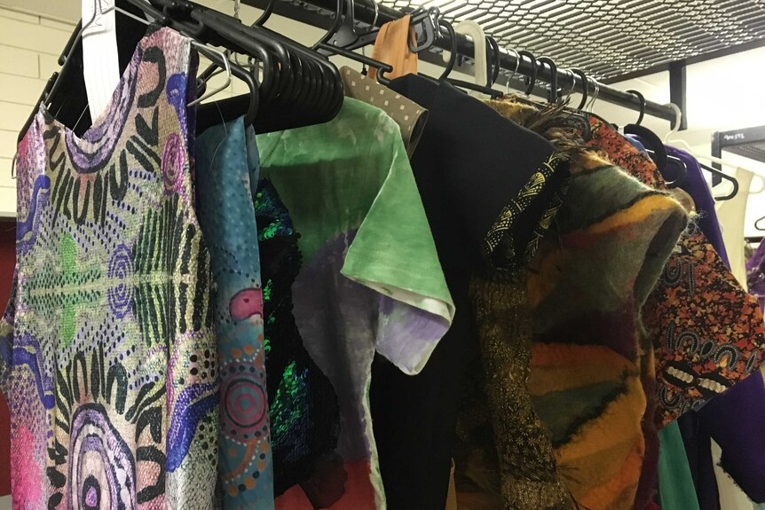 Colourful garments, many with Aboriginal prints, hang from a clothing rack