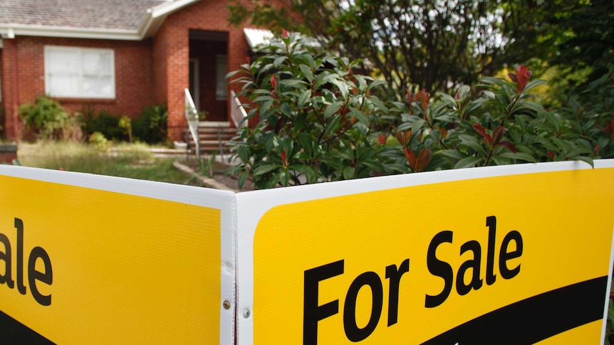 A house with a black and yellow for sale sign in front of it.