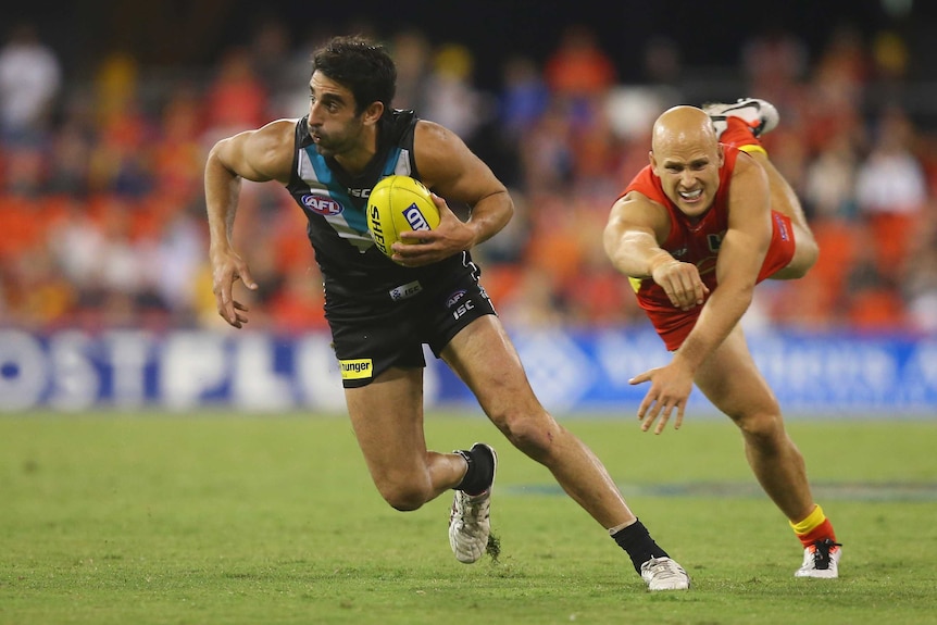 Port Adelaide's Domenic Cassisi runs from Gold Coast's Gary Ablett at Metricon.