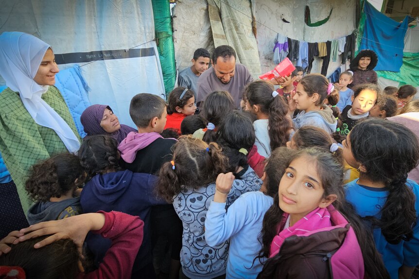 A young girl looks over her shoulder among a crowd of children gathered around a man.