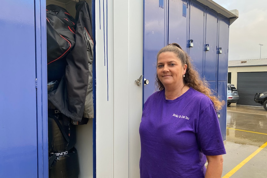 A woman stands next to a row of lockers, including one which is open.