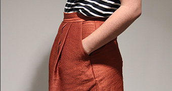 A woman wearing a skirt stands with her hands in her pockets.