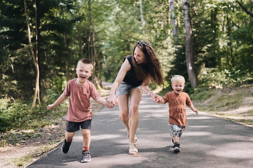 Danielle is running along a path through the bush with her two young kids. They're all laughing. 