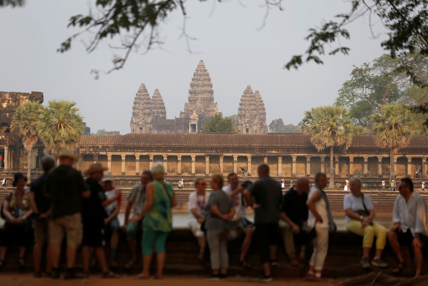 tourists sit in the shade, in the background you can see the temples of Angkor Wat.