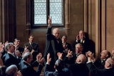A scene from Darkest Hour with Winston Churchill holding up a two fingered peace salute in front of a crowd of cheering men.