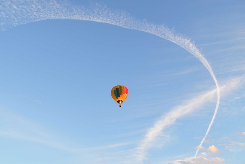Hot air balloon flies by a contrail.