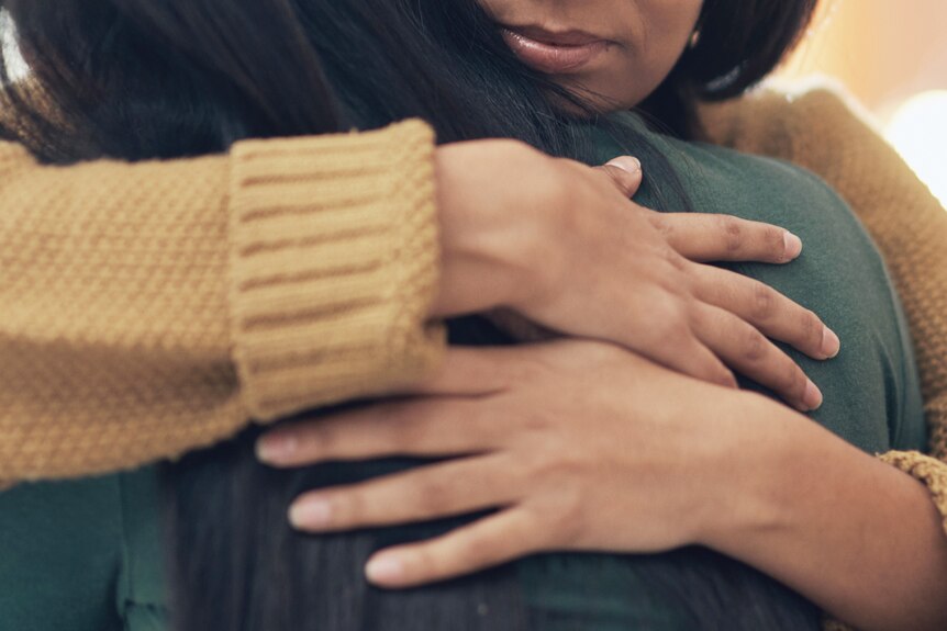 Two people hugging with a close up of hands coming together as they envelope another person in a hug