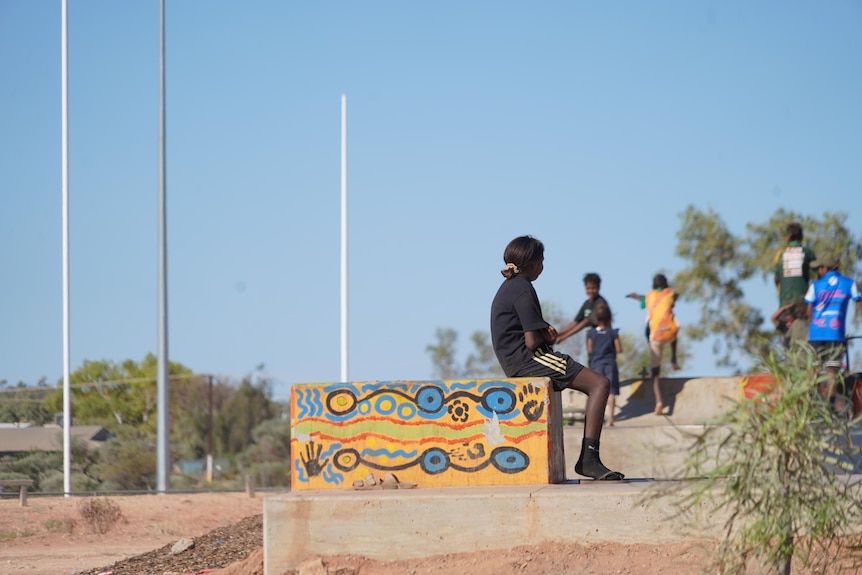 Aboriginal children sit and stand at a colourful skate park