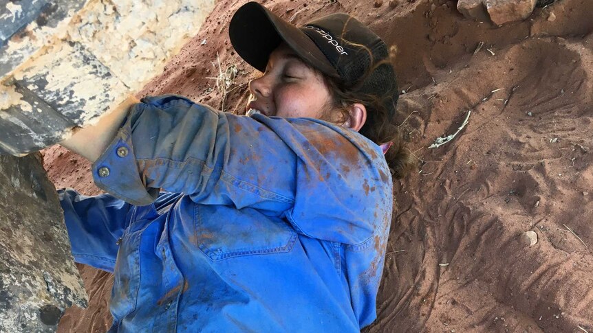 Woman lying in red dirt under truck with tools ion hand.