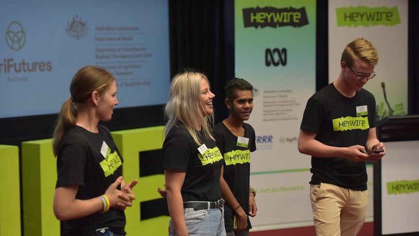 Four young people are on stage in Heywire shirts