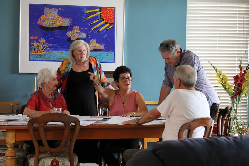 group of people sitting and standing around a table with lots of paperwork