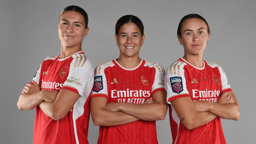 Three women soccer players wearing red and white cross their arms for a portrait photo