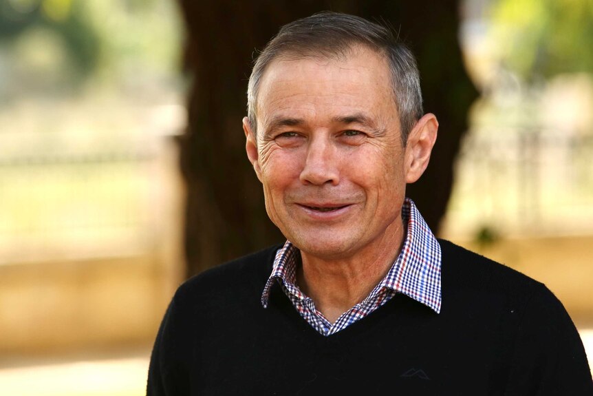 Roger Cook wears a blue, white and red checked shirt under a black sweater and smiles
