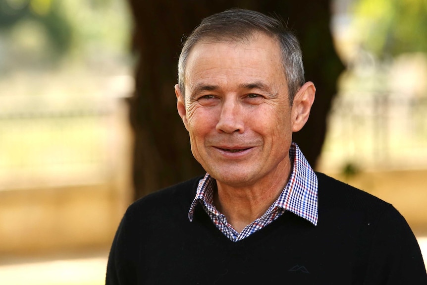 Roger Cook wears a blue, white and red checked shirt under a black sweater and smiles